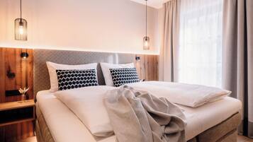 A modern hotel room with a large bed, wooden headboard, and a nightstand with a lamp.
