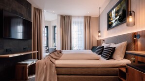 Une chambre d’hôtel moderne avec un grand lit, un téléviseur à écran plat, un banc en bois et un tableau au mur.