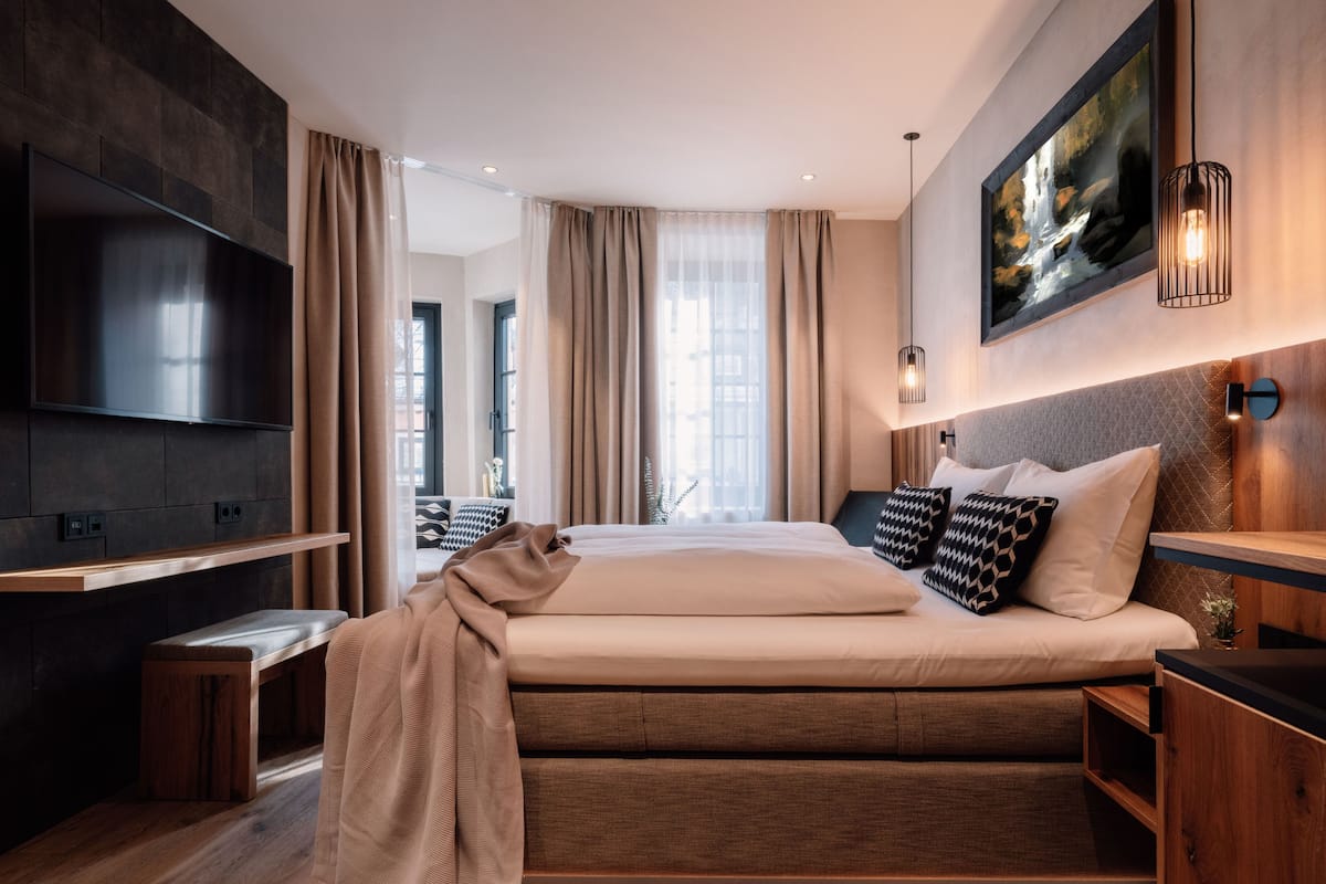 Une chambre d’hôtel moderne avec un grand lit, un téléviseur à écran plat, un banc en bois et un tableau au mur.