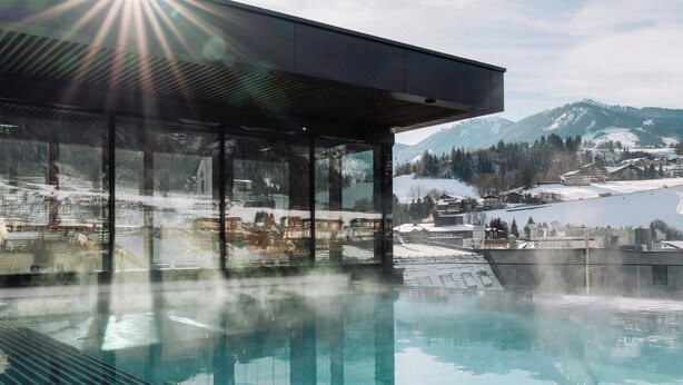 Un bâtiment moderne doté de grandes fenêtres en verre donnant sur un paysage enneigé et sur un bassin dont la surface reflète l’environnement.