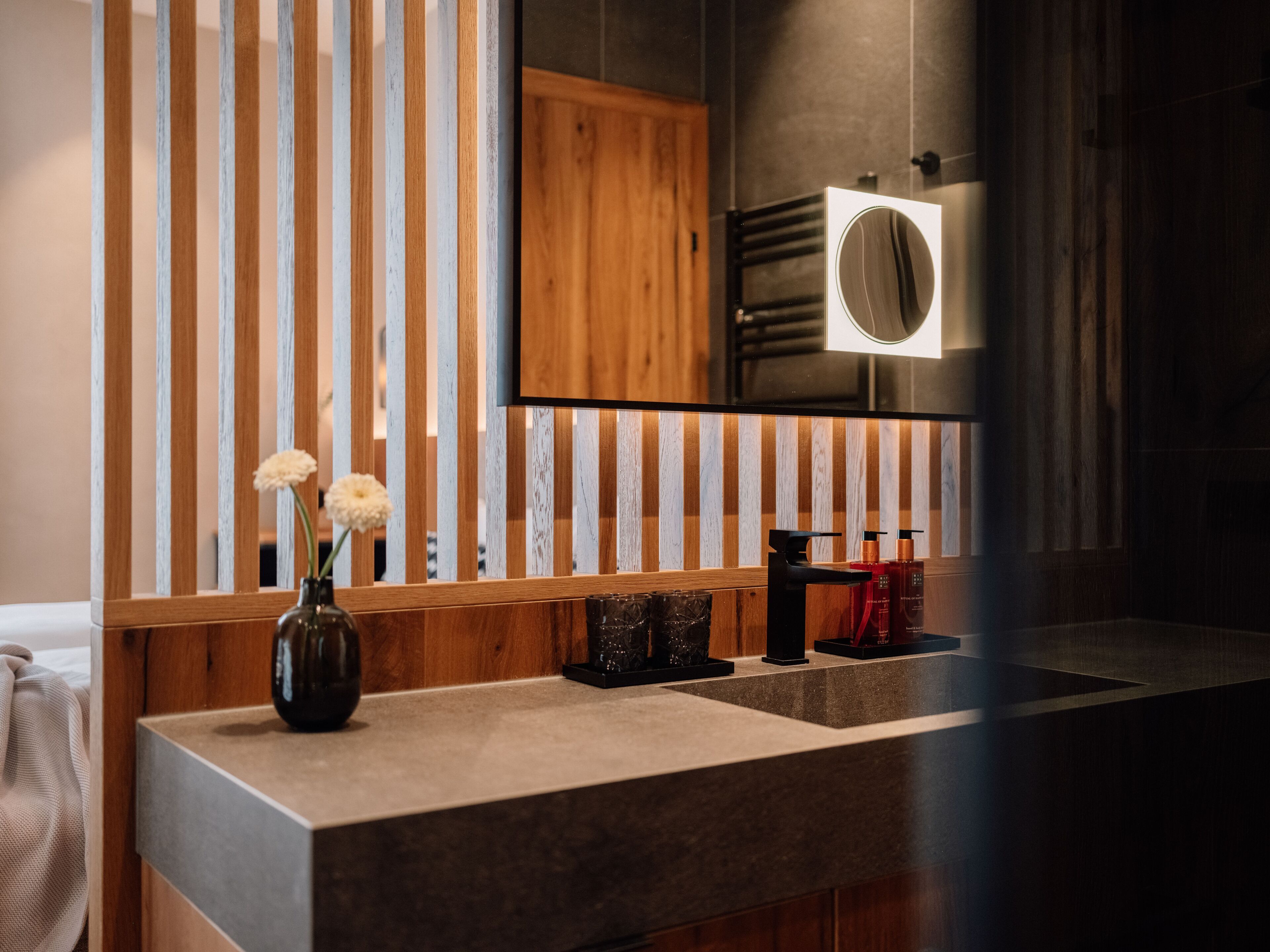 Un baño moderno con tocador de madera, un espejo y un florero con flores.