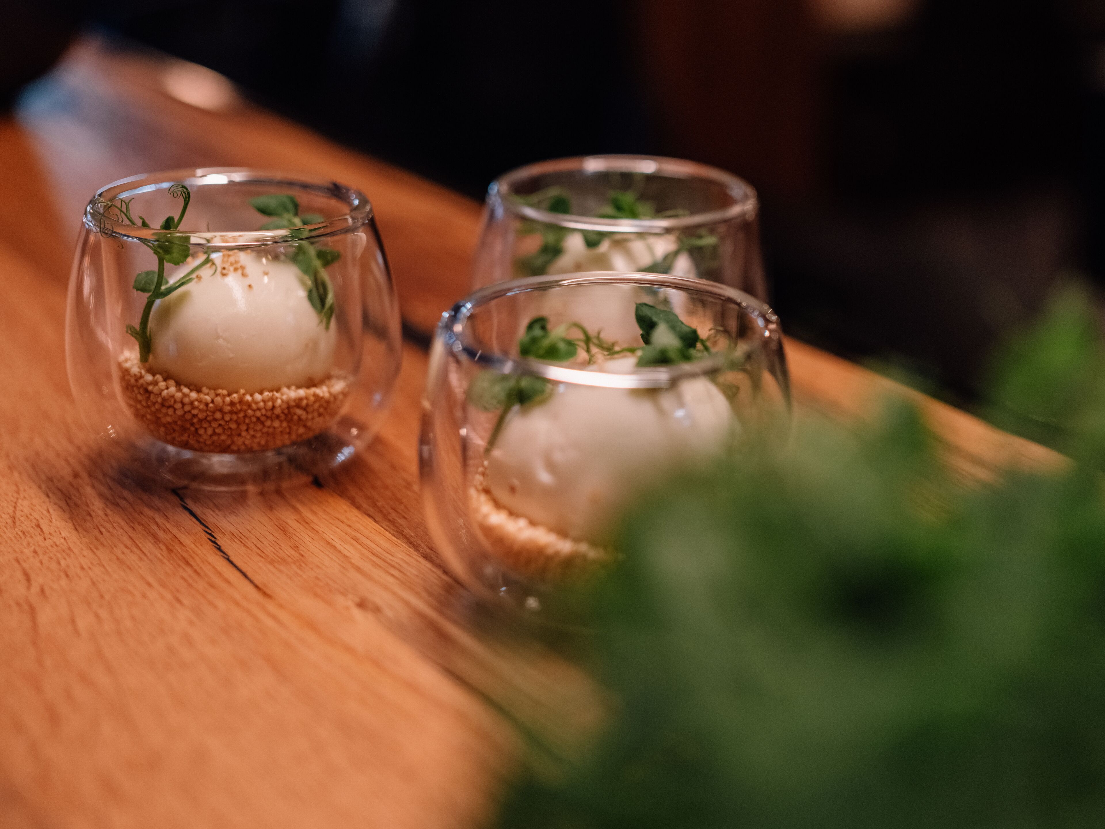 Two clear glass vases with a white object and green garnish on a wooden surface.