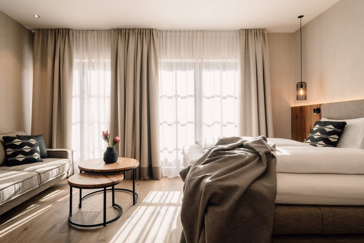 Une chambre d’hôtel avec un lit, un canapé, une petite table ronde et un vase rempli de fleurs.