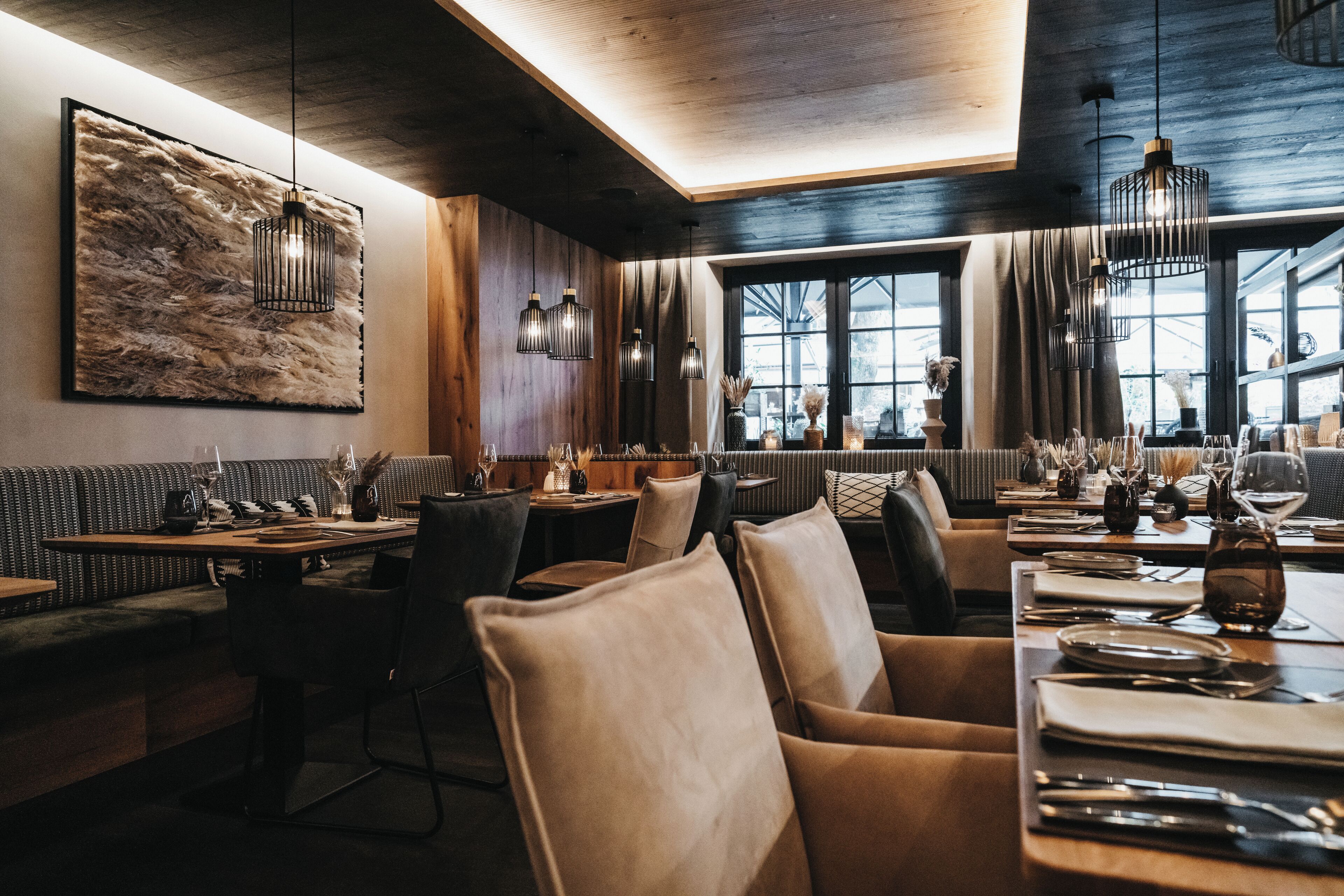 Ein Restaurantinneres mit Holzwänden, einem großen abstrakten Gemälde und mehreren gedeckten Tischen mit Gläsern und Besteck.