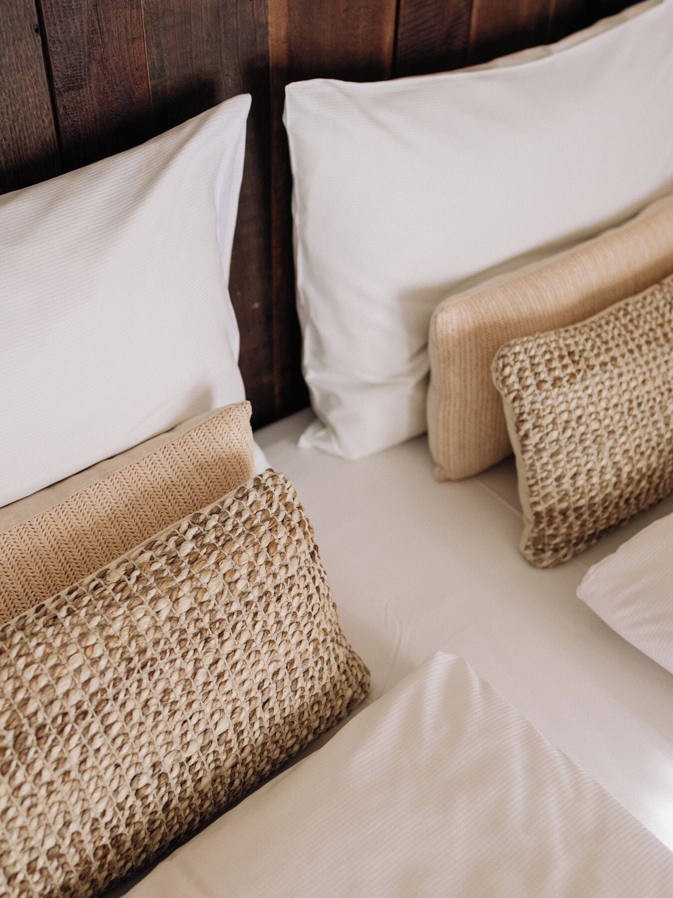 A bed with white linens and two beige, textured pillows.