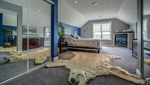 Un dormitorio con un espejo grande, una cama, una alfombra de pieles y una chimenea.