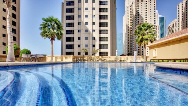 A swimming pool with clear blue tiles, surrounded by tall buildings and palm trees. - Maison Privee - Premium Studio Apt in the Heart of JBR Beach, Dubai (Dubai)
