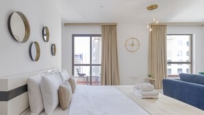 A hotel room with a large bed, a blue armchair, a small table with a plant, and a view of the city through the window. - Maison Privee - Premium Studio Apt in the Heart of JBR Beach, Dubai (Dubai)