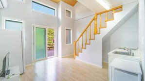 Un'ampia stanza con una scala in legno, una porta scorrevole in vetro che dà su uno spazio esterno e un angolo cottura con lavello e piano di lavoro.