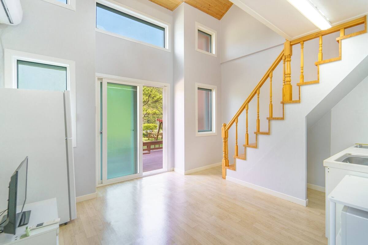 A spacious room with a wooden staircase, a sliding glass door leading to an outdoor area, and a kitchenette with a sink and countertop.