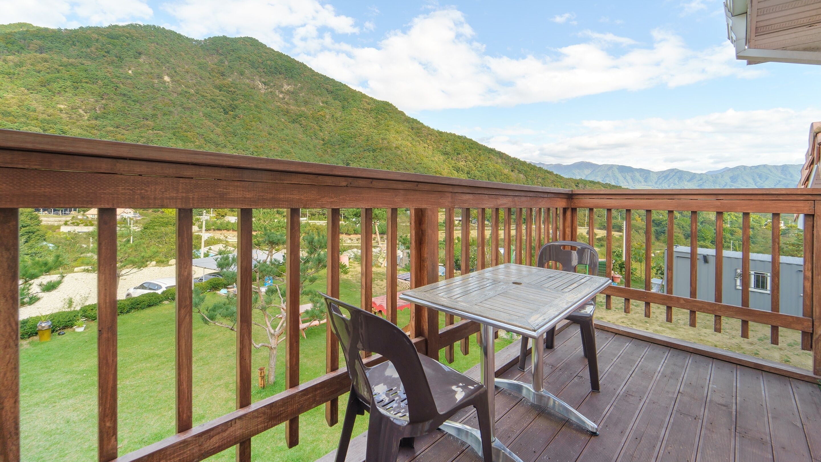 Una terraza de madera con mesa y sillas, con vista a un paisaje montañoso.