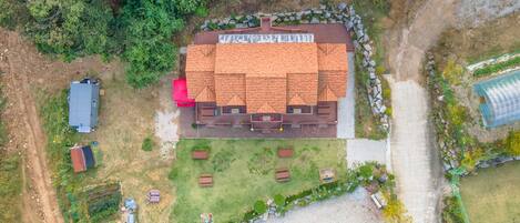 An aerial view of a house with a tiled roof, a fenced yard, and a greenhouse.