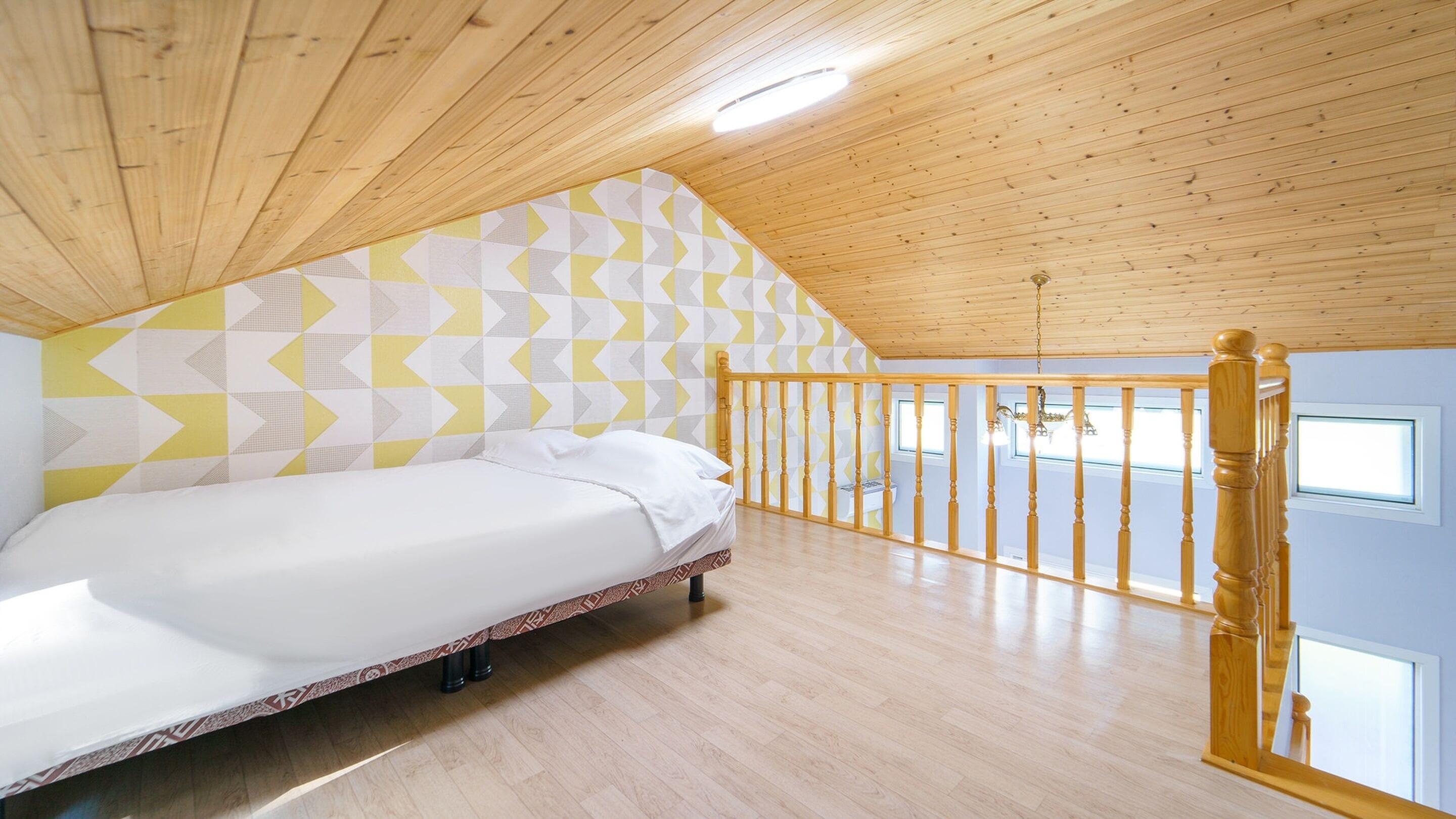 A bedroom with a bed, wooden ceiling, geometric-patterned wall, and a balcony with a railing.