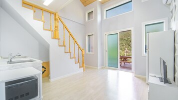 Amplia habitación con escalera de madera, zona de cocina y puerta corrediza de vidrio que da a una terraza exterior.