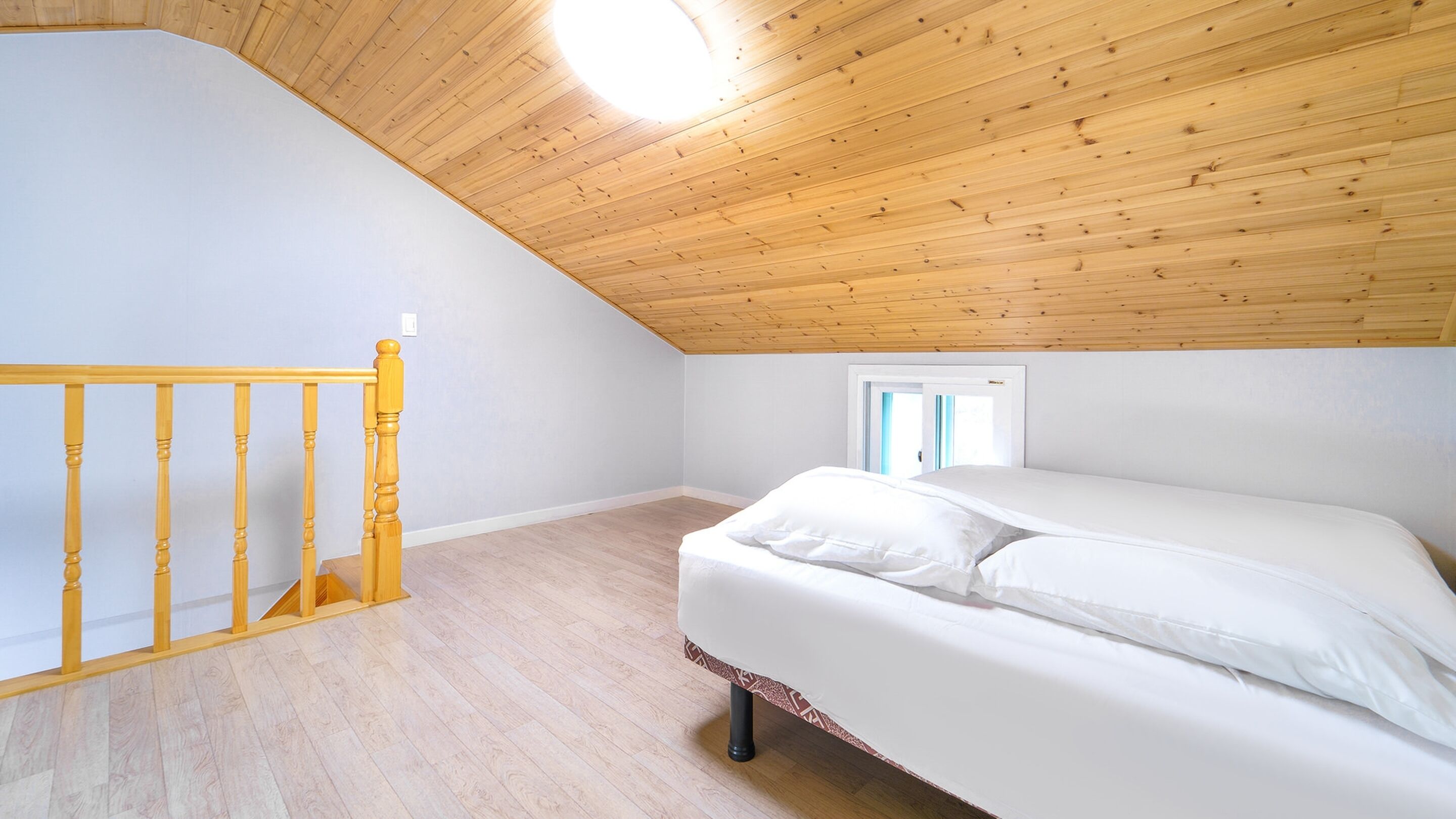 A bedroom with a sloped ceiling, a wooden staircase, a bed with white bedding, and a window with curtains.