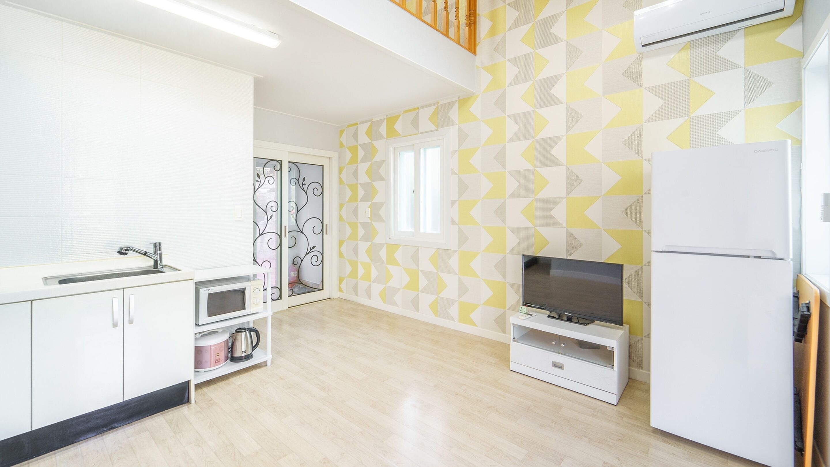 A modern kitchen with white cabinets, a microwave, a kettle, and a built-in TV.