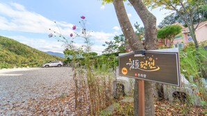 Un cartello con testo coreano, una strada sterrata, un'auto parcheggiata e un paesaggio montuoso.