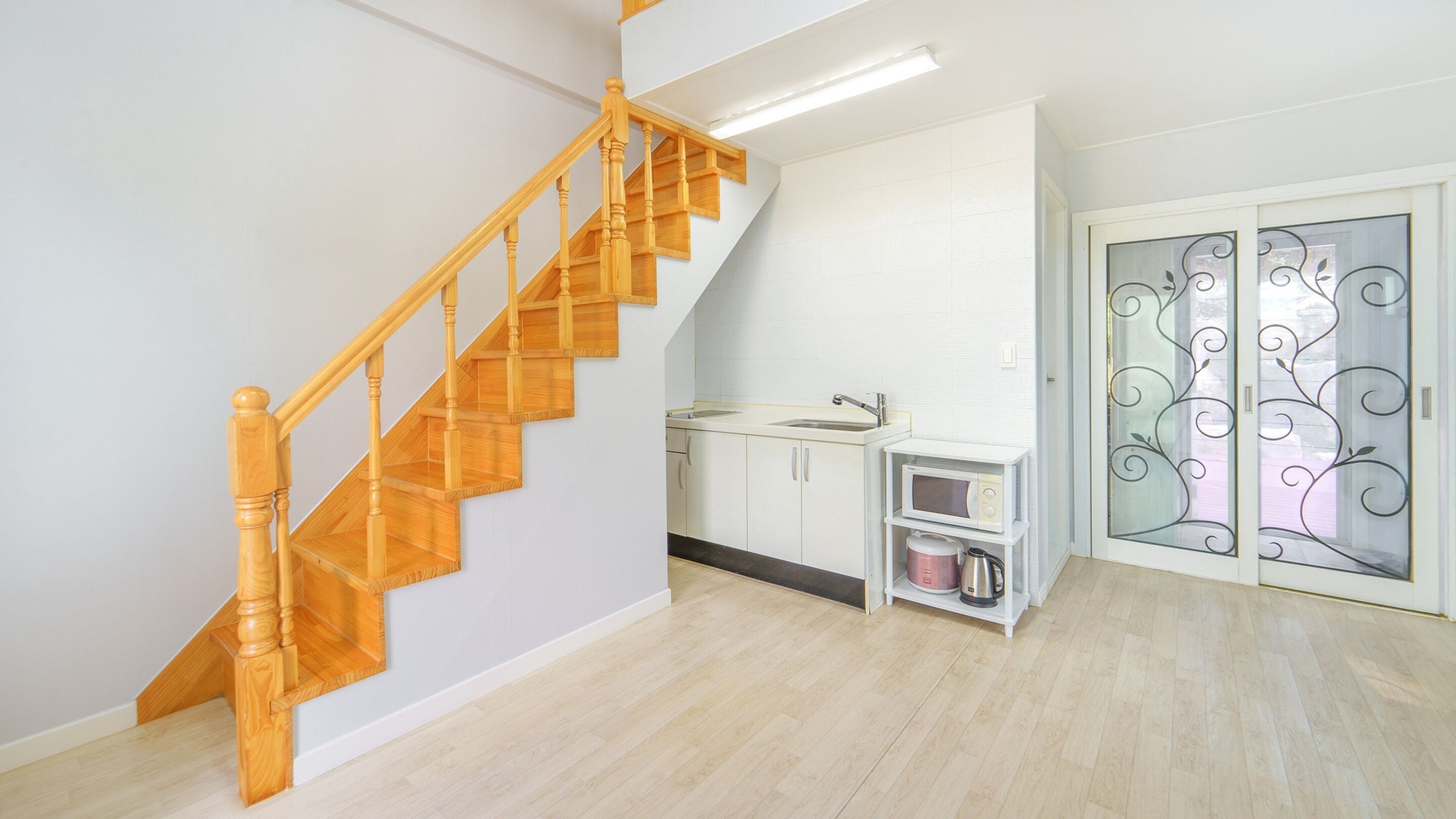 A staircase with wooden balusters leading to a landing, a kitchen area with white cabinets and a microwave, and a glass door with decorative patterns.