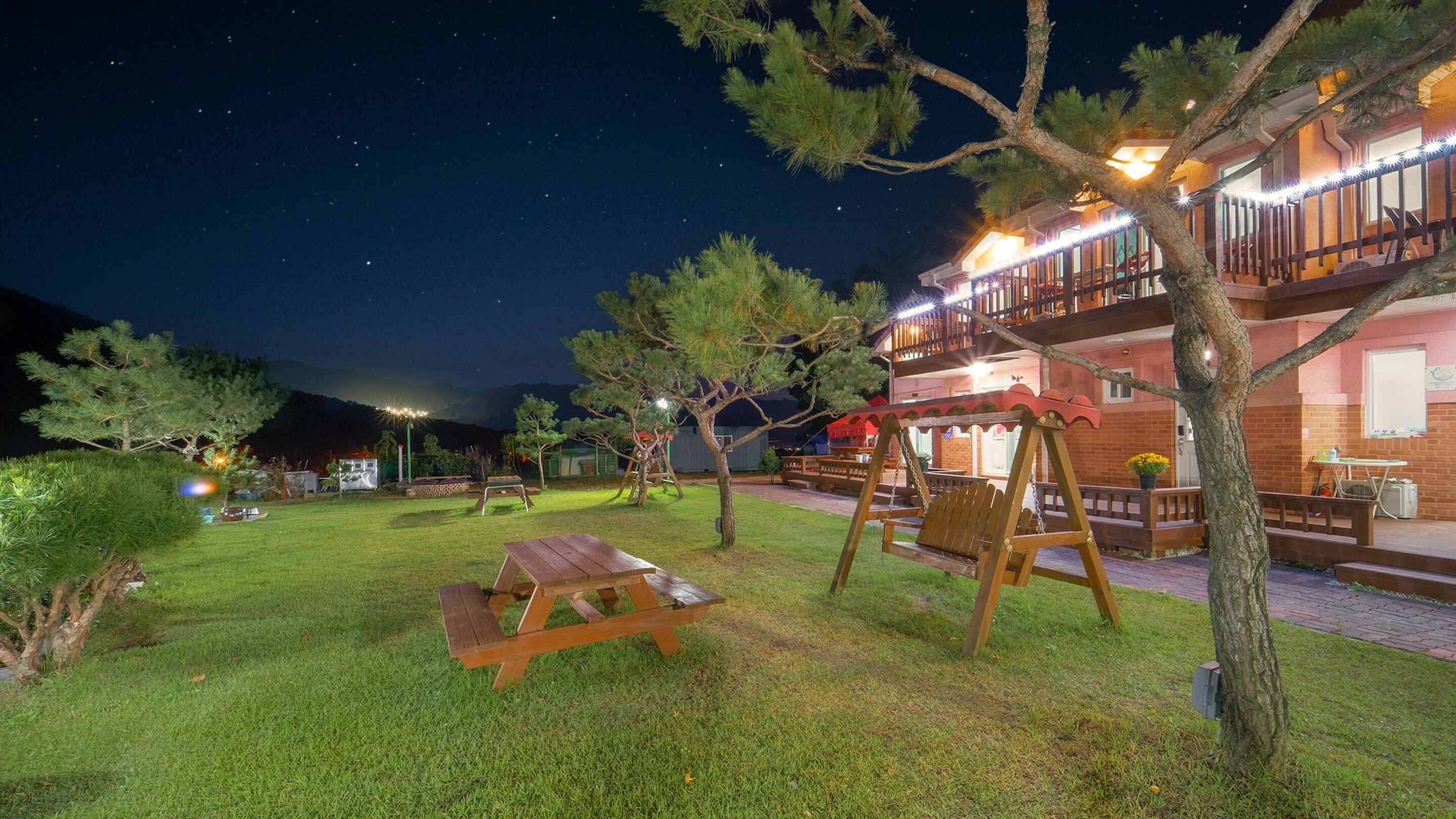 A well-lit outdoor area with a picnic table, a swing set, and a building with a balcony.