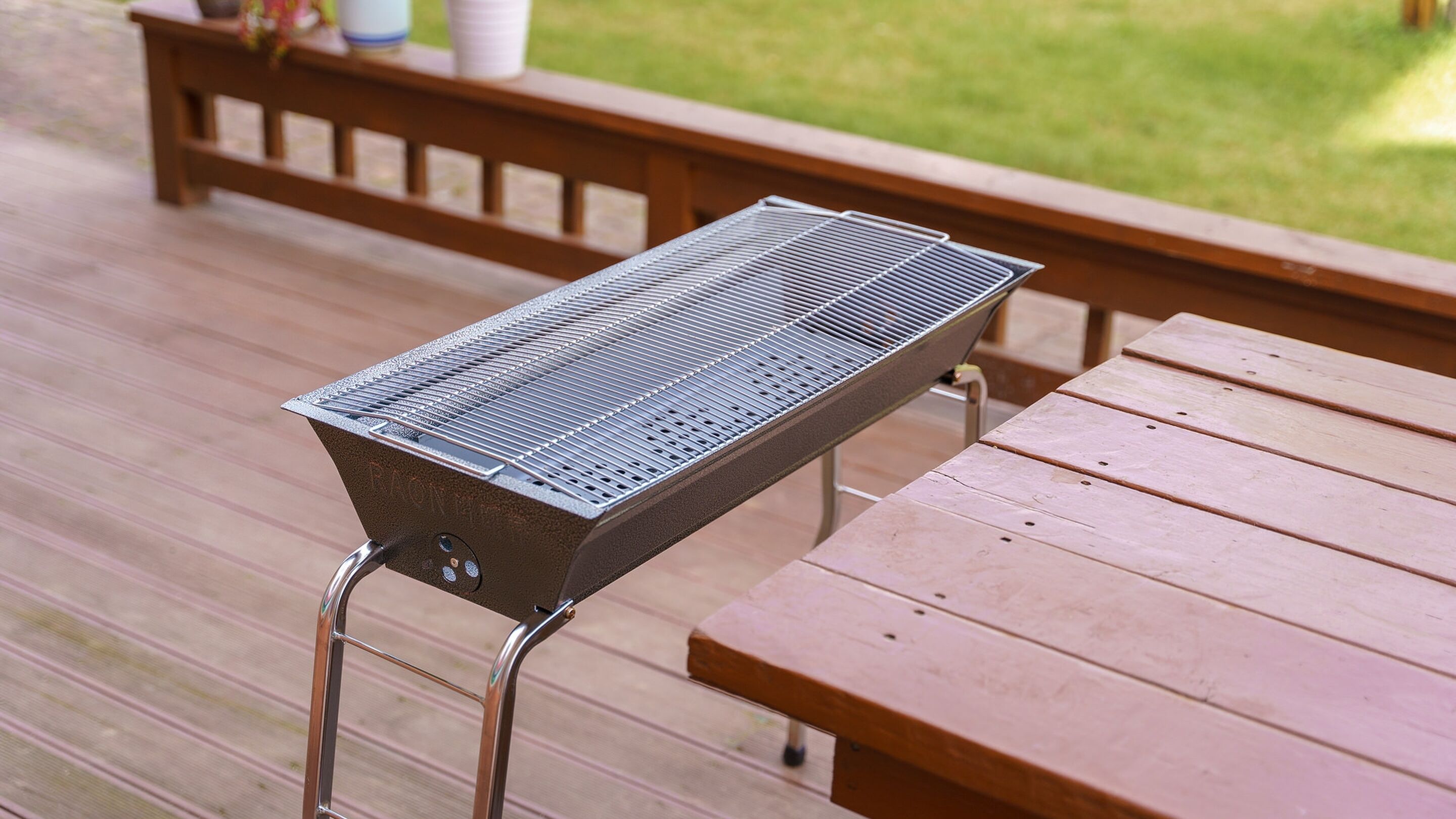 Una parrilla portátil sobre una terraza de madera con un banco al fondo.