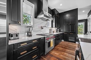 A modern kitchen with black cabinets, a marble countertop, a built-in oven, and a window with a view of greenery.