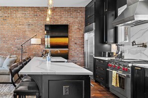 A modern kitchen with a brick wall, a large island, and a stove.