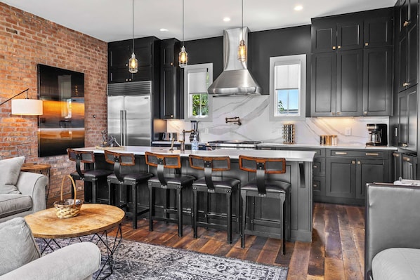 A modern kitchen with a central island, bar stools, and a seating area with a coffee table.