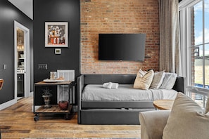A modern living room with a brick wall, a flat-screen TV, a sofa, and a view of the outdoors.