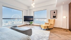 A modern hotel room with large windows, a TV, a sofa, a chair, and a floor lamp. - Maison Privee - Sun Sand & Dubai Luxury at JBR Beach (Dubai)