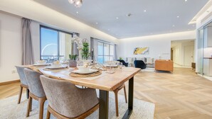 A spacious dining area with a wooden table and chairs, large windows offering a view of the city, and a modern chandelier. - Maison Privee - Sun Sand & Dubai Luxury at JBR Beach (Dubai)