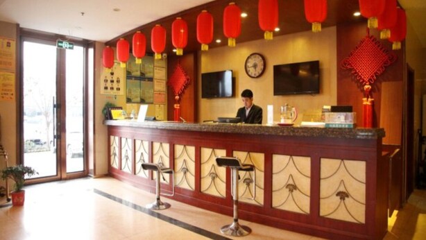 A hotel reception area with a counter, bar stools, red lanterns, a clock, and a television. - Greentree Inn Heze Juye West No.1 Middle School Hotel (Heze)