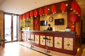 A hotel reception area with a counter, bar stools, red lanterns, a clock, and a television. - Greentree Inn Heze Juye West No.1 Middle School Hotel (Heze)