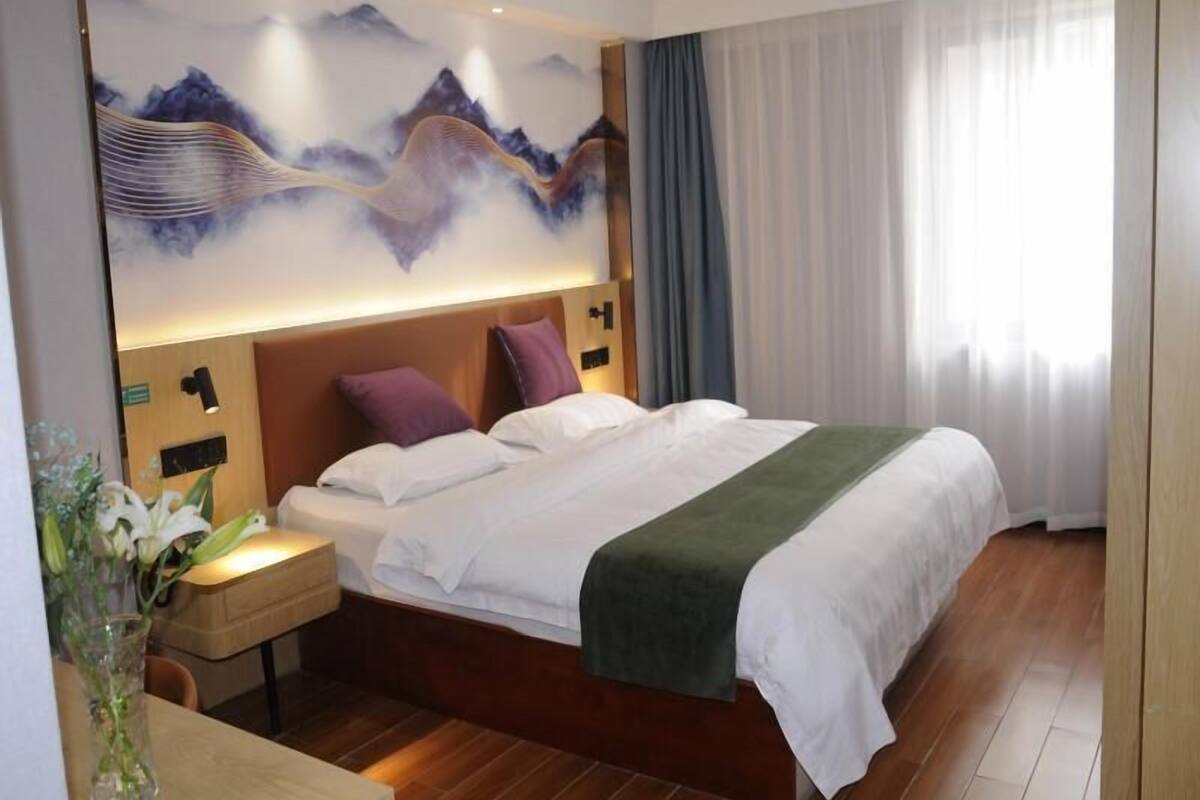 Una habitación de hotel con una cama grande, una mesita de noche, un florero con flores y un mural en la pared.