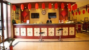 Un espace d’accueil d’hôtel avec un comptoir, deux tabourets de bar, une horloge et des lanternes rouges.