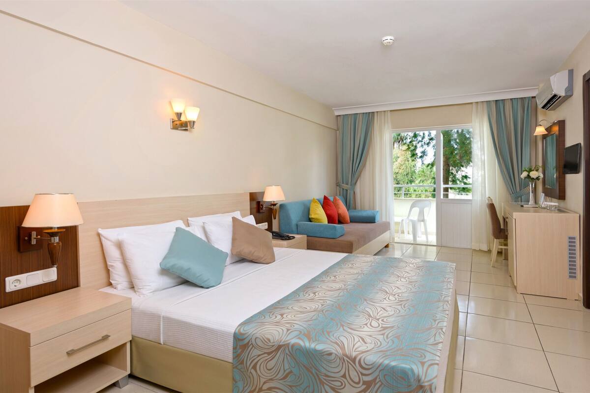 A hotel room with a bed, bedside tables, a sofa, a desk, and a view of the outdoors.