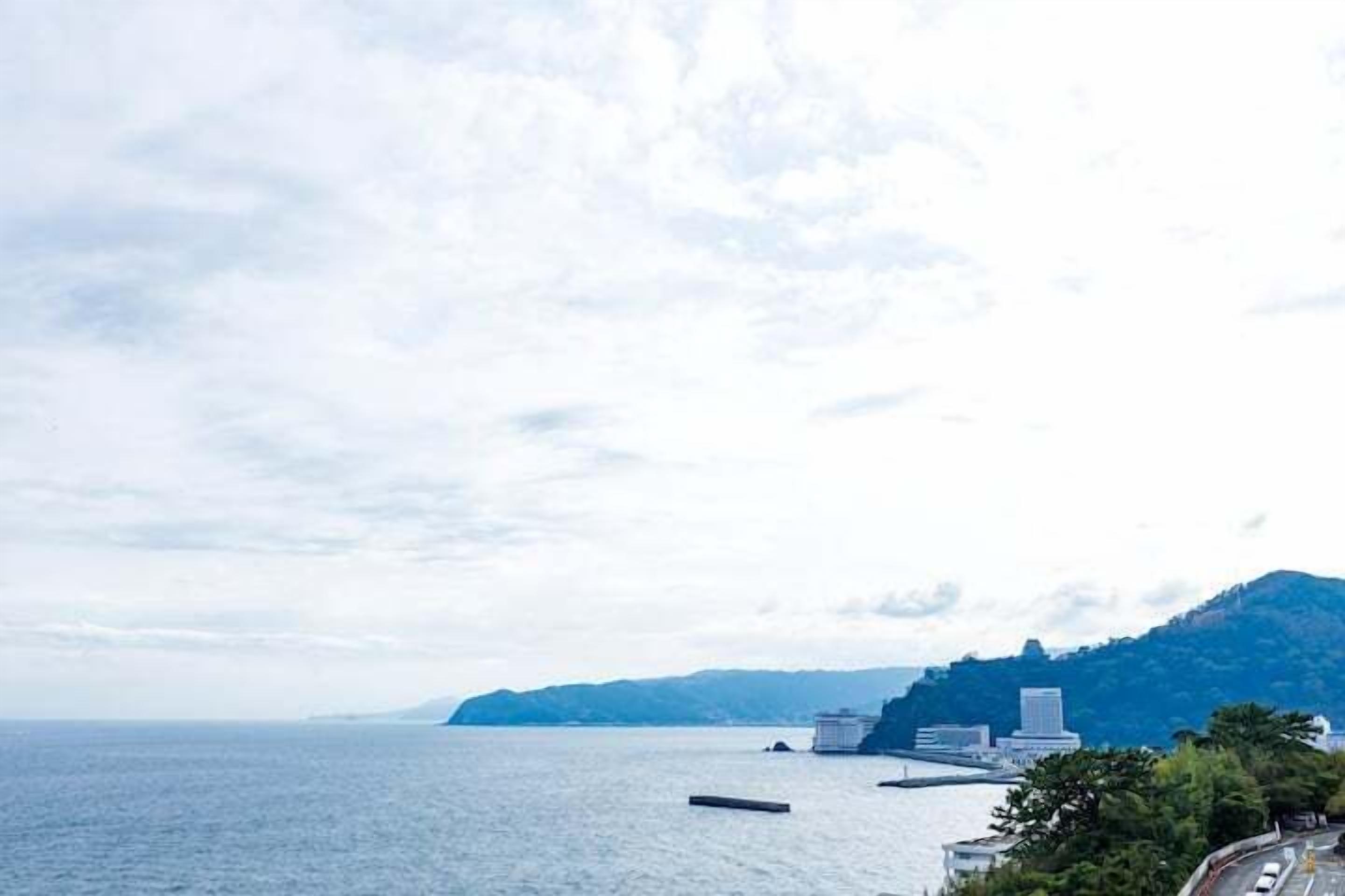 A coastal view with a road leading to a building, a body of water, and a hill in the background.