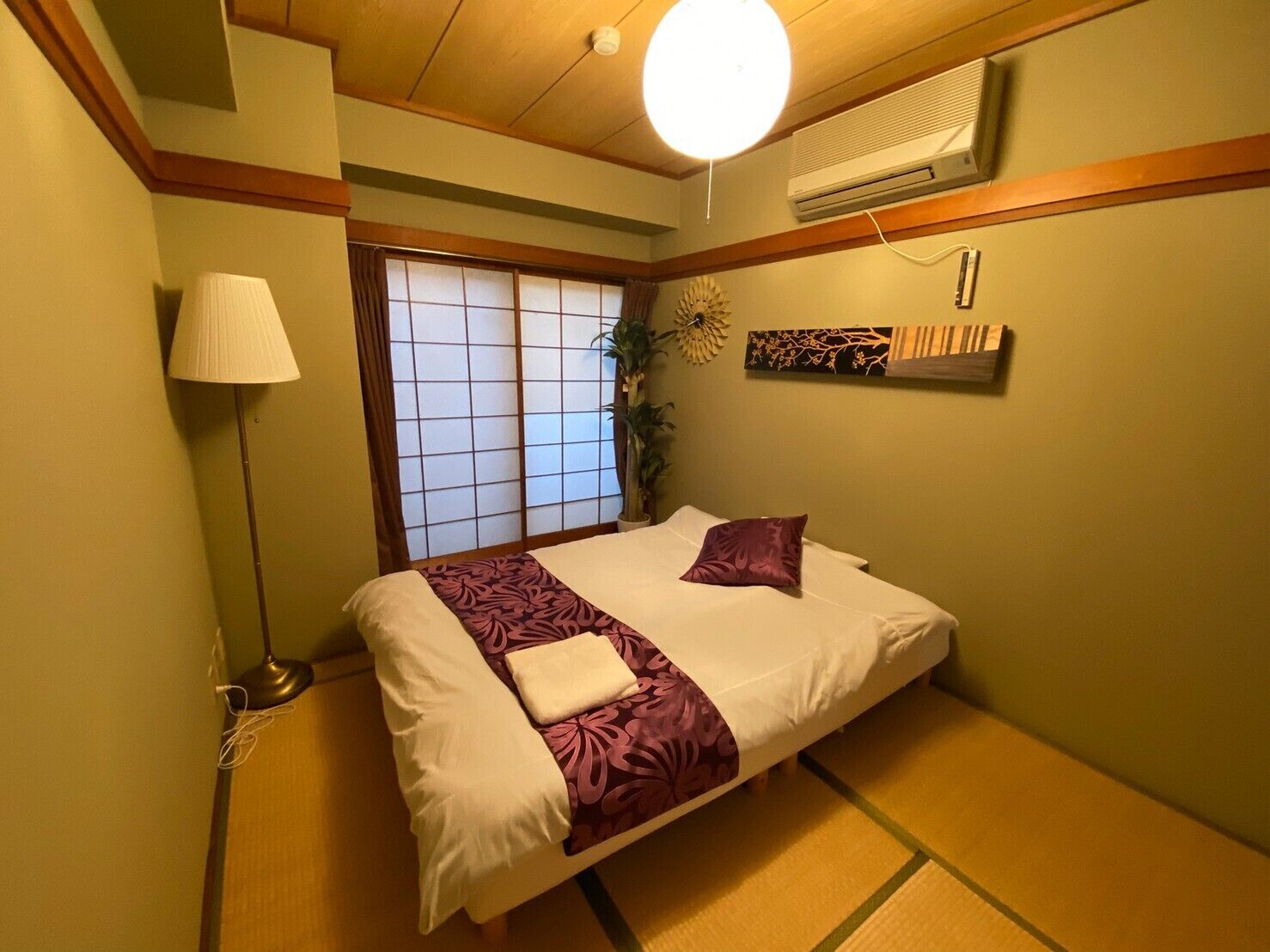 A traditional Japanese-style bedroom with tatami flooring, a bed with a purple and white bedspread, a shoji screen window, and a ceiling fan.