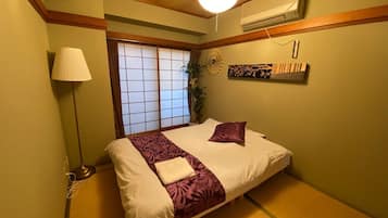 A traditional Japanese-style bedroom with tatami flooring, a bed with a purple and white bedspread, a shoji screen window, and a ceiling fan.