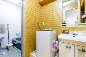 A bathroom with wooden panel walls, a white sink with a mirror, and a shower area. - Atami Kaikotei 202 (Atami)