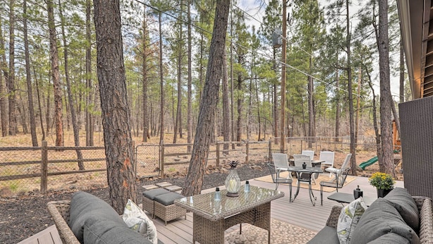 A deck with wicker furniture, a glass-top table, and a view of a forest. - Renovated Cottage w/ Fire Pit in Munds Park! (Munds Park)
