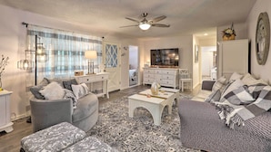 A living room with a sofa, armchair, coffee table, and a TV. There is a ceiling fan and a window with curtains. - Renovated Cottage w/ Fire Pit in Munds Park! (Munds Park)