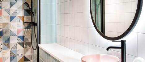 A bathroom with a patterned shower wall, a round mirror, and a pink sink.