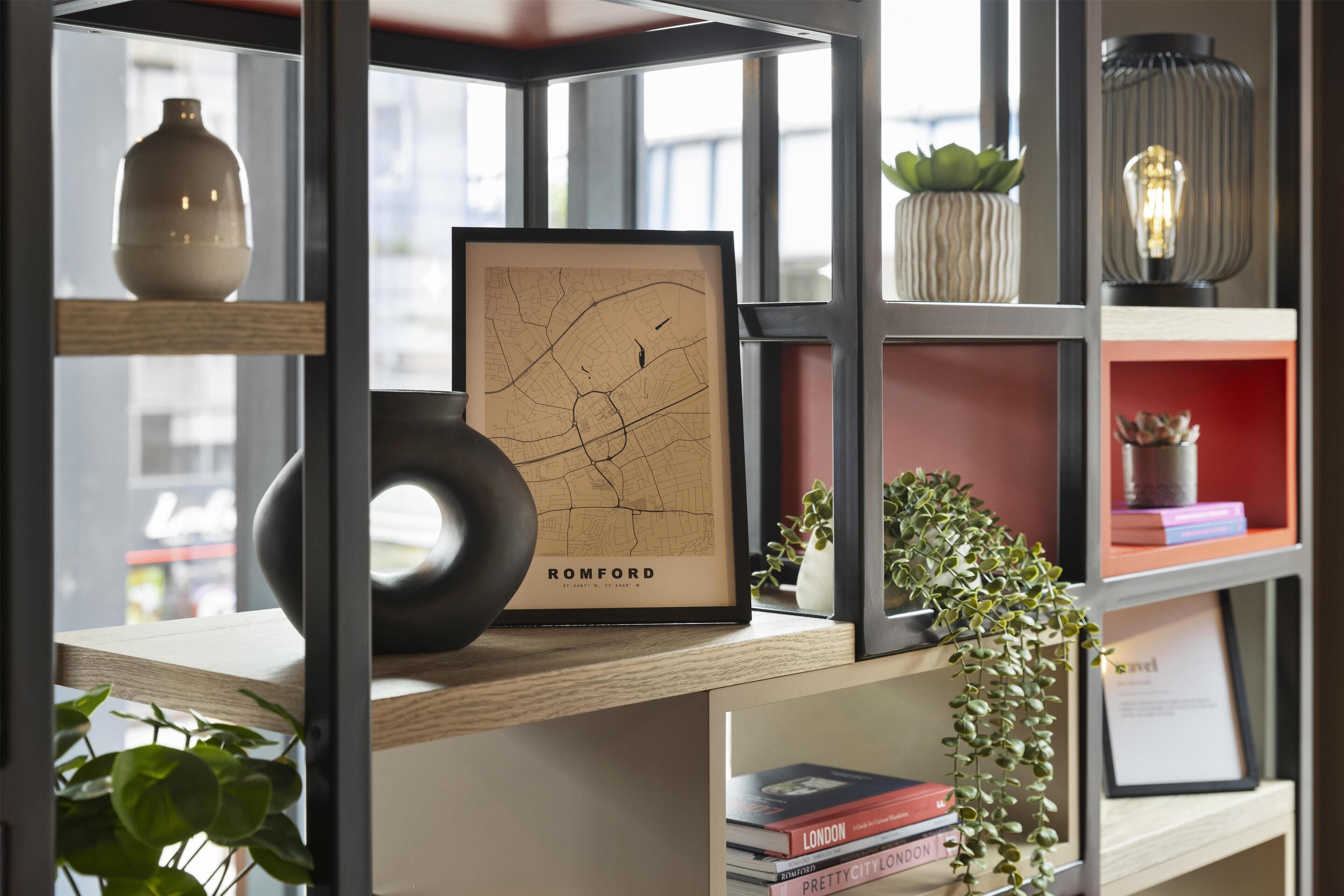 Una estantería con un mapa enmarcado de Romford, libros y objetos decorativos.