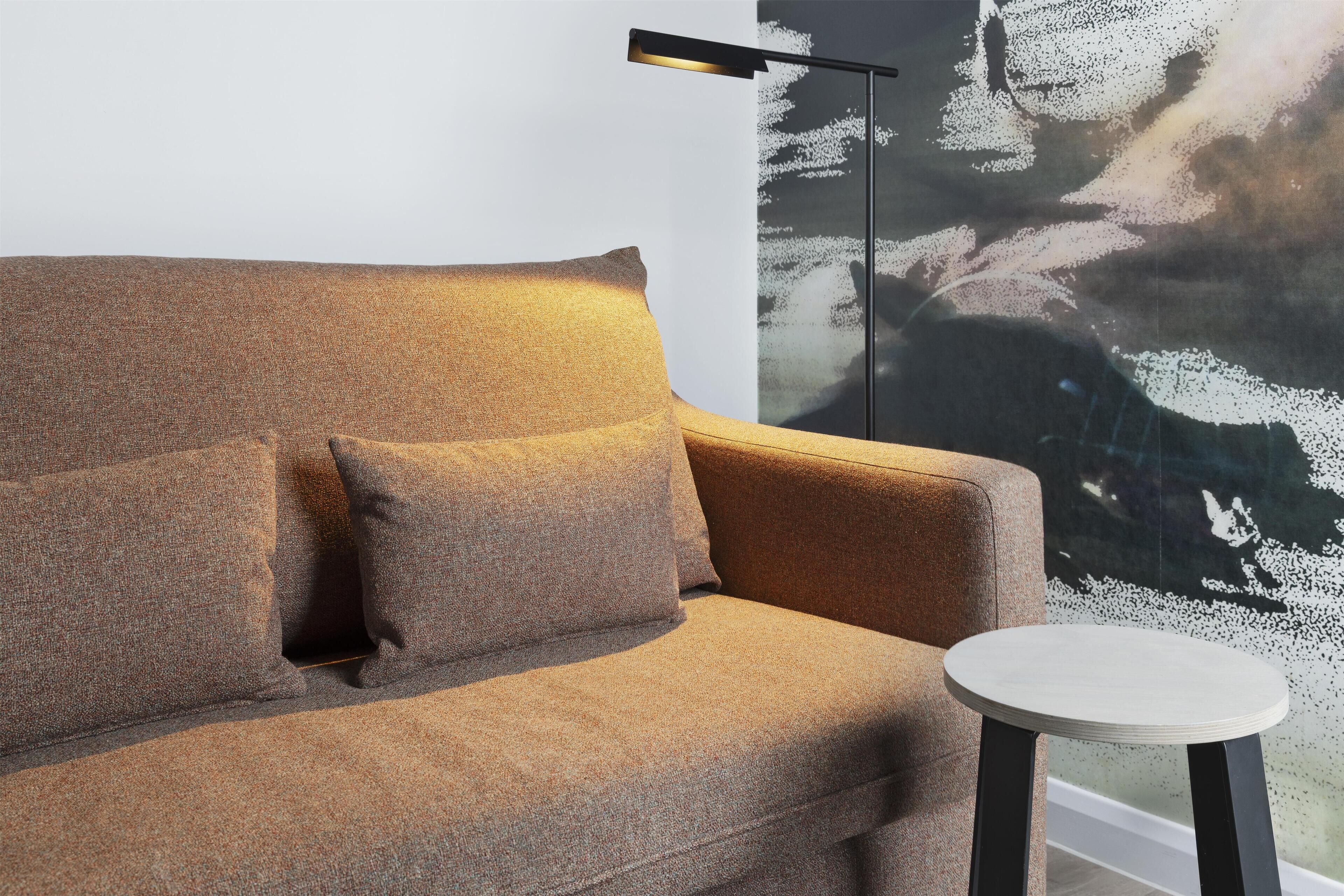 A modern living room with a sofa and a small round table, a floor lamp, and a wall with a textured abstract painting.