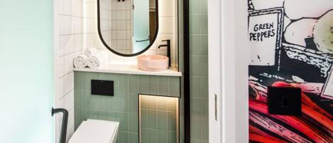 A bathroom with a white toilet, a round mirror, a pink sink, and green-tiled walls.