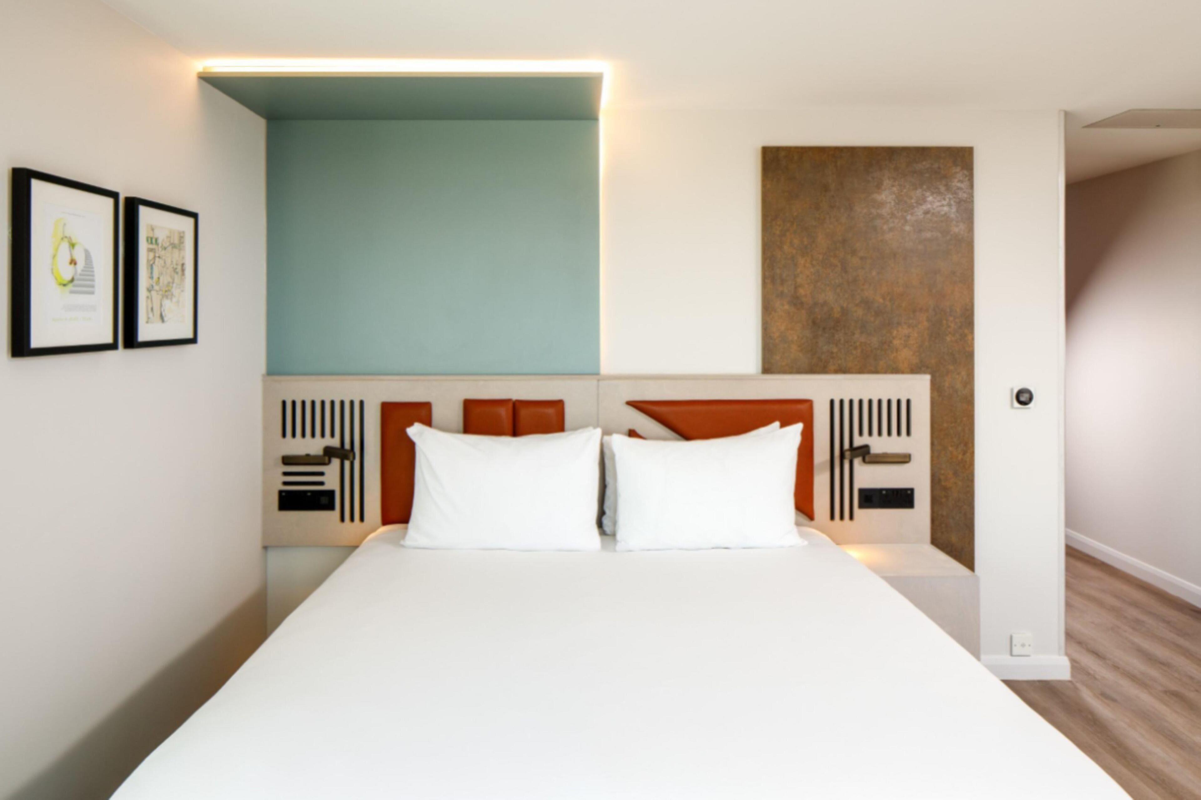A modern hotel room with a large bed, white bedding, a wooden headboard, and a light blue accent wall.