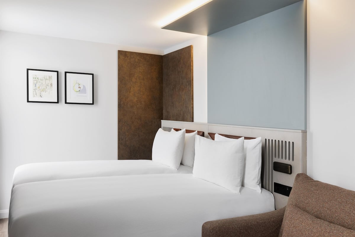 A modern hotel room with a large bed, a headboard with vertical slats, and two framed artworks on the wall.