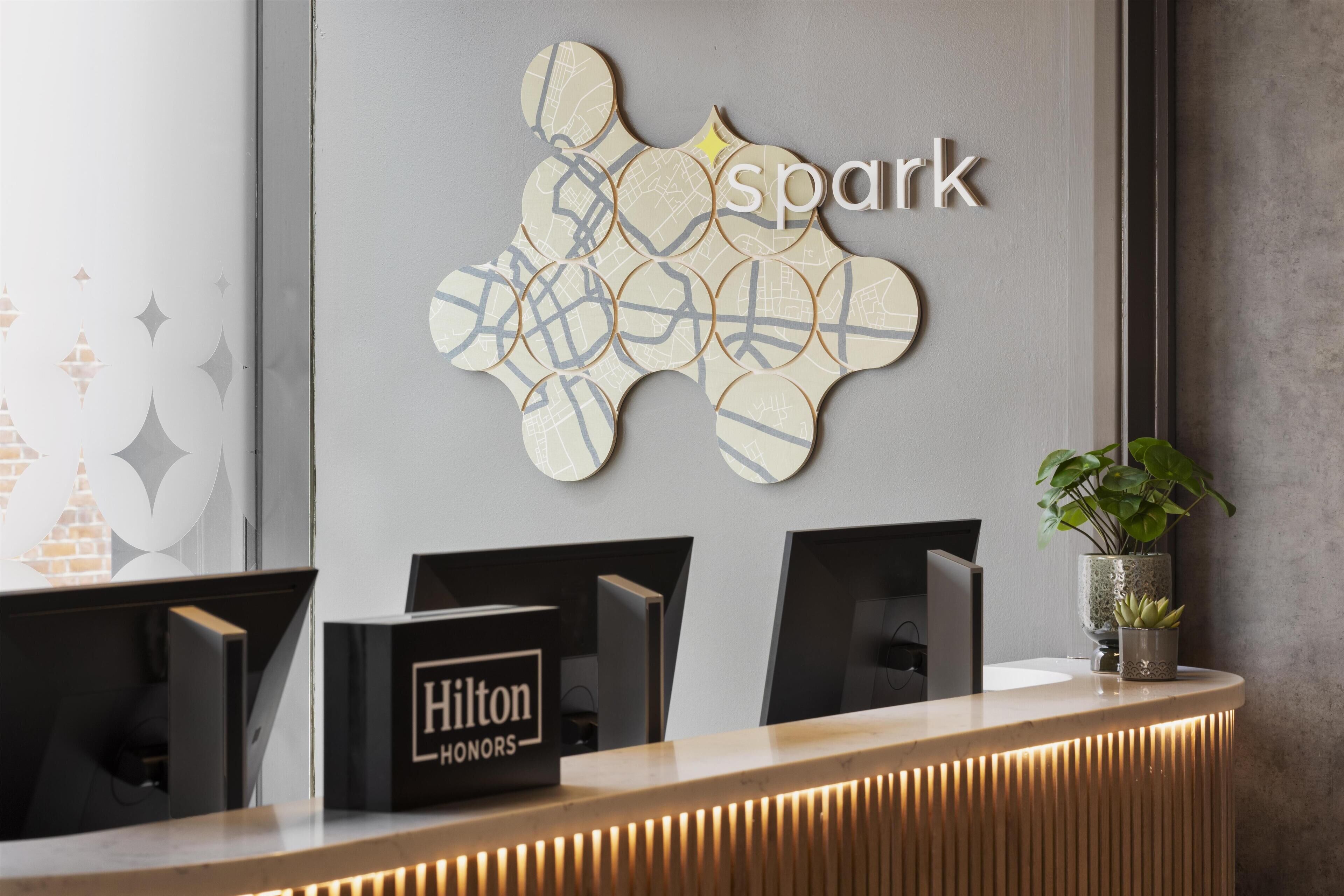 A hotel reception desk with a map artwork, a Hilton Honors sign, and a potted plant.