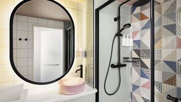 Un baño con un espejo redondo, un lavabo con una pileta color beige y una ducha con un diseño de azulejos geométricos.