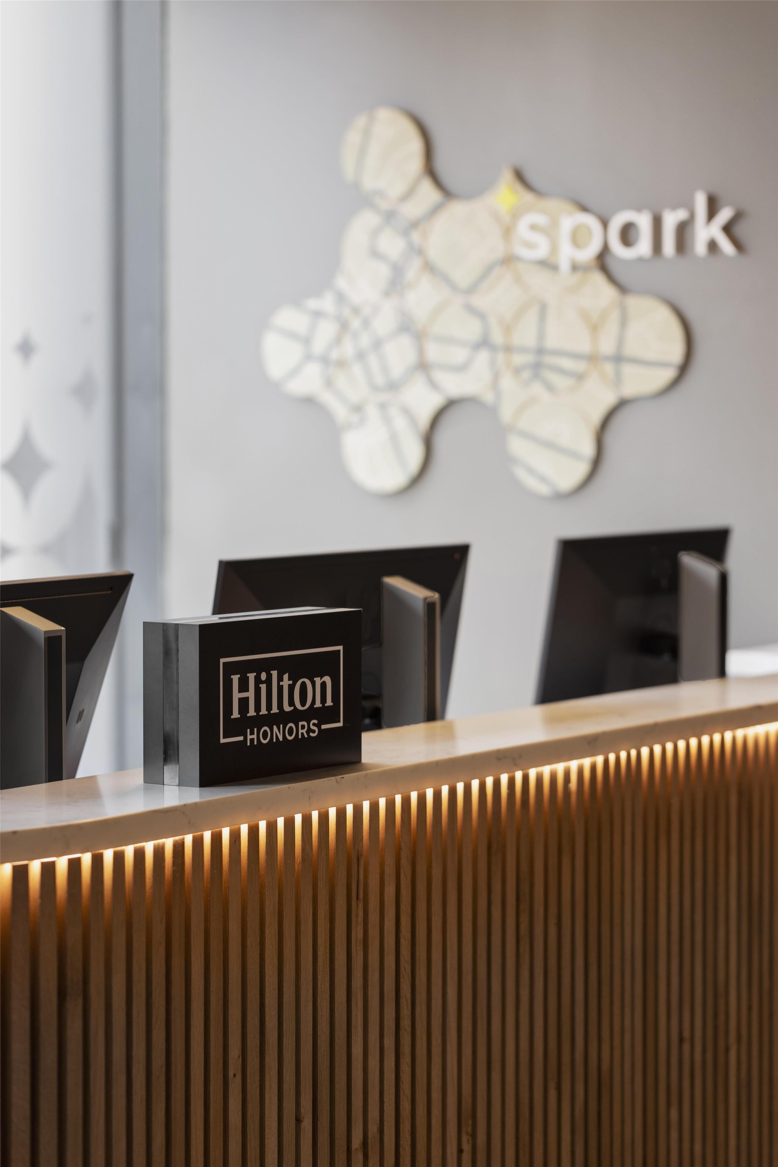 A reception desk with a 'Hilton Honors' sign, a 'spark' logo, and a modern, minimalist design with vertical wooden slats.
